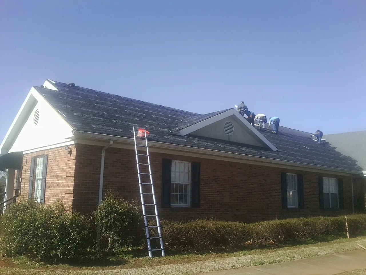 Crew tearing shingles off a brick ranch roof with a ladder set — Metal Roof Repair work by our crew in Lugoff