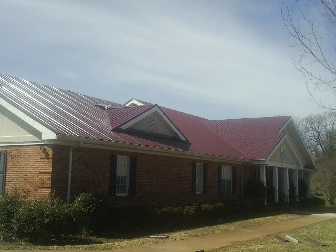 Red metal roof with gabled entries on a long brick building, from a Hail Damage Roof Repair job in Lugoff