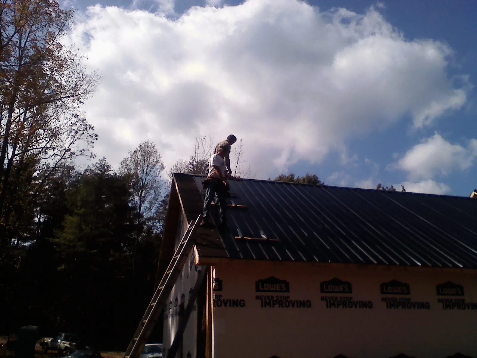 Roofer fastening dark metal panels high against a cloudy sky, from a Roof Inspection job in Lugoff